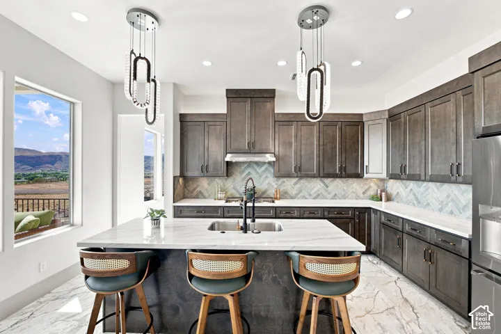 Spacious kitchen featuring dark wood-finish cabinetry, a large kitchen island with a sink, white stone countertops, and a herringbone tile backsplash