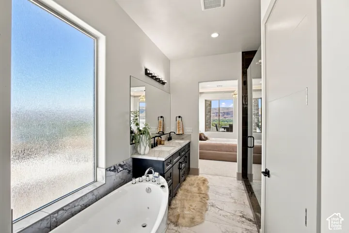 Freestanding jetted bathtub with a marble surround, dual vanity with undermount sinks and black fixtures, and a spacious glass-enclosed shower