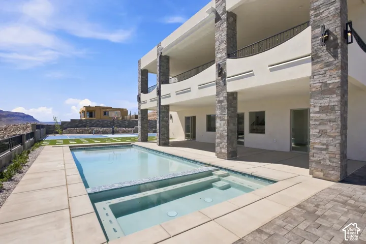 Expansive outdoor living area featuring a swimming pool, integrated spa, and an artificial turf sports court