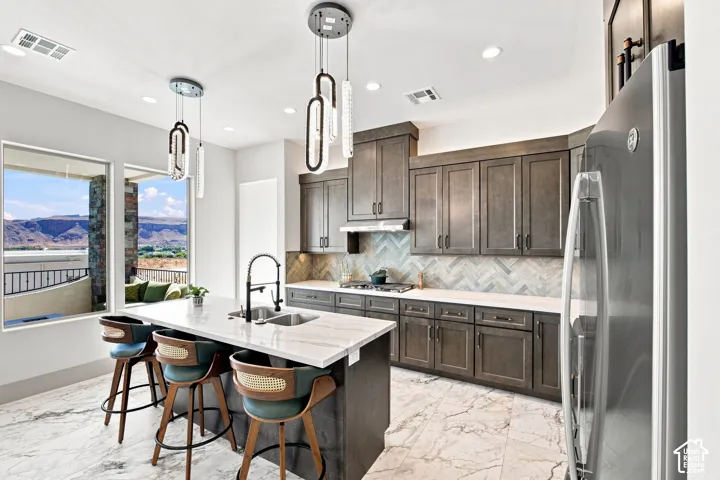 Contemporary kitchen featuring a large island with an undermount sink, a herringbone tile backsplash, gray cabinetry, and stainless steel appliances