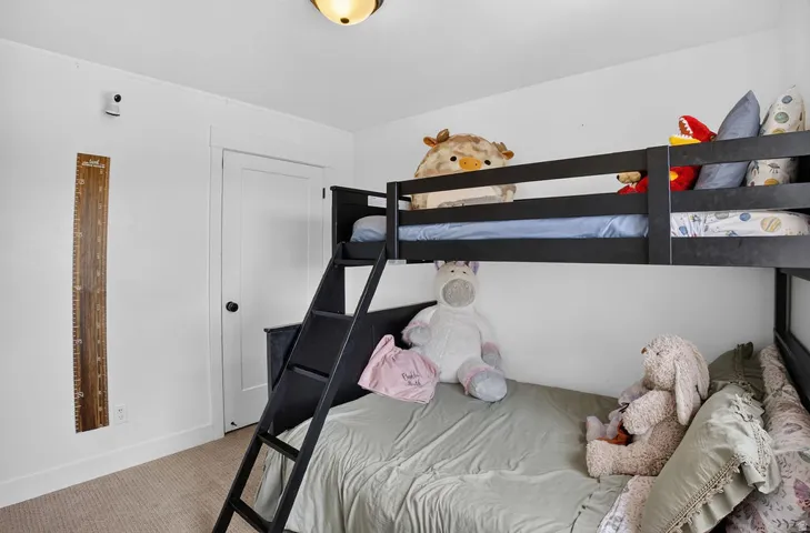 Carpeted bedroom featuring a white door with a black knob, white baseboards, and a semi-flush mount ceiling light fixture