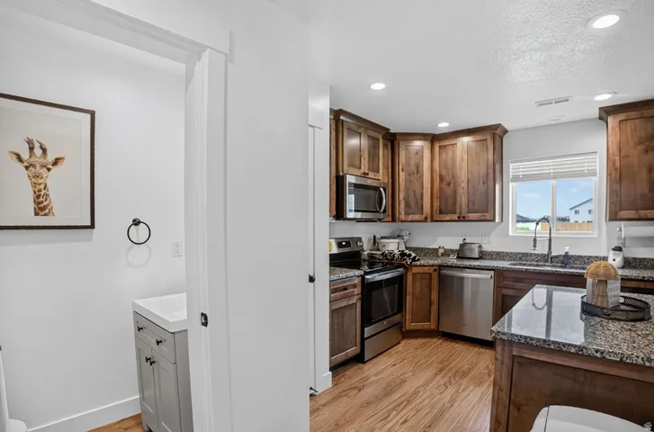 Contemporary kitchen featuring wood cabinetry, stainless steel appliances, speckled stone countertops, and wood-finish flooring