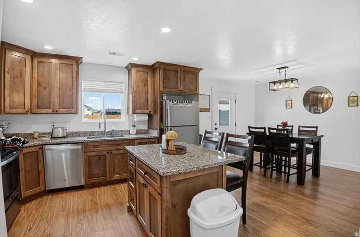 Kitchen featuring wood-finish flooring, stainless steel appliances, and a central island with a granite-style countertop
