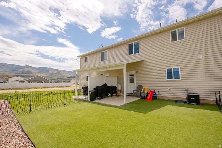Rear exterior featuring two levels of windows, a covered patio, and a fenced yard with artificial turf