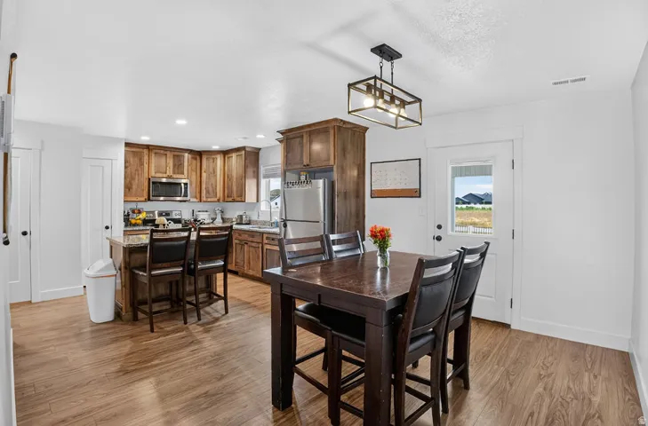 Open-concept kitchen and dining area featuring wood-finish flooring, recessed lighting, and a modern rectangular chandelier
