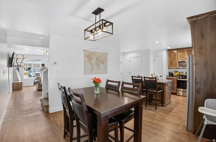 Open-concept dining area with wood-finish flooring, featuring a contemporary linear chandelier and recessed lighting
