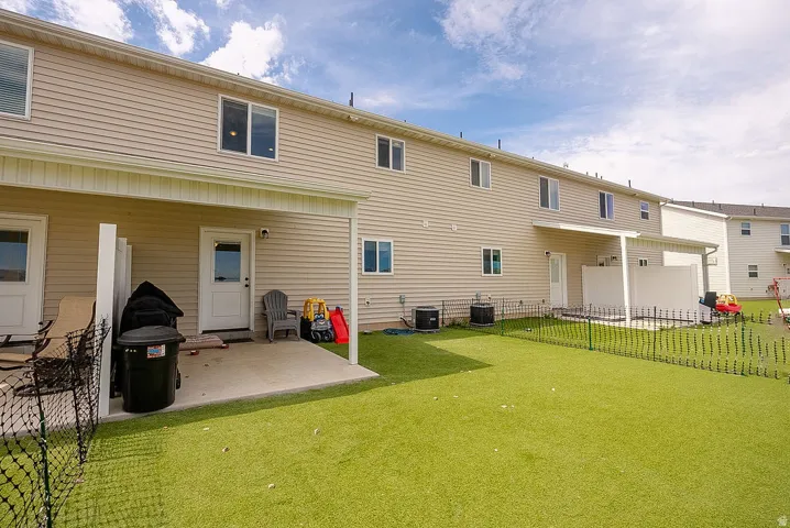 Expansive green artificial turf backyard featuring a concrete patio with an overhead awning and a low black metal fence