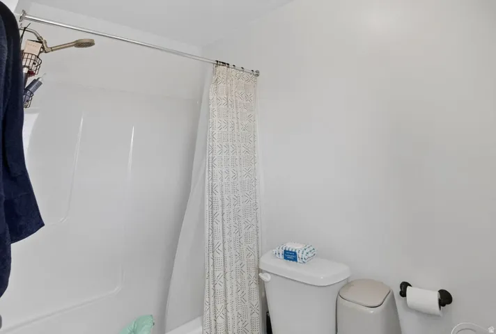 Bright bathroom featuring a white tub-shower combination with a handheld shower head, a white toilet, and a wall-mounted toilet paper holder