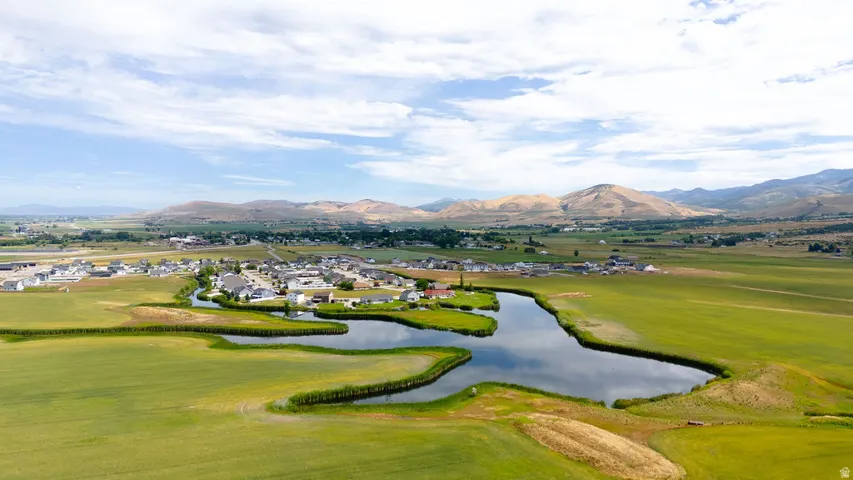 Aerial perspective showcasing a community situated alongside a reflective body of water, surrounded by expansive green fields