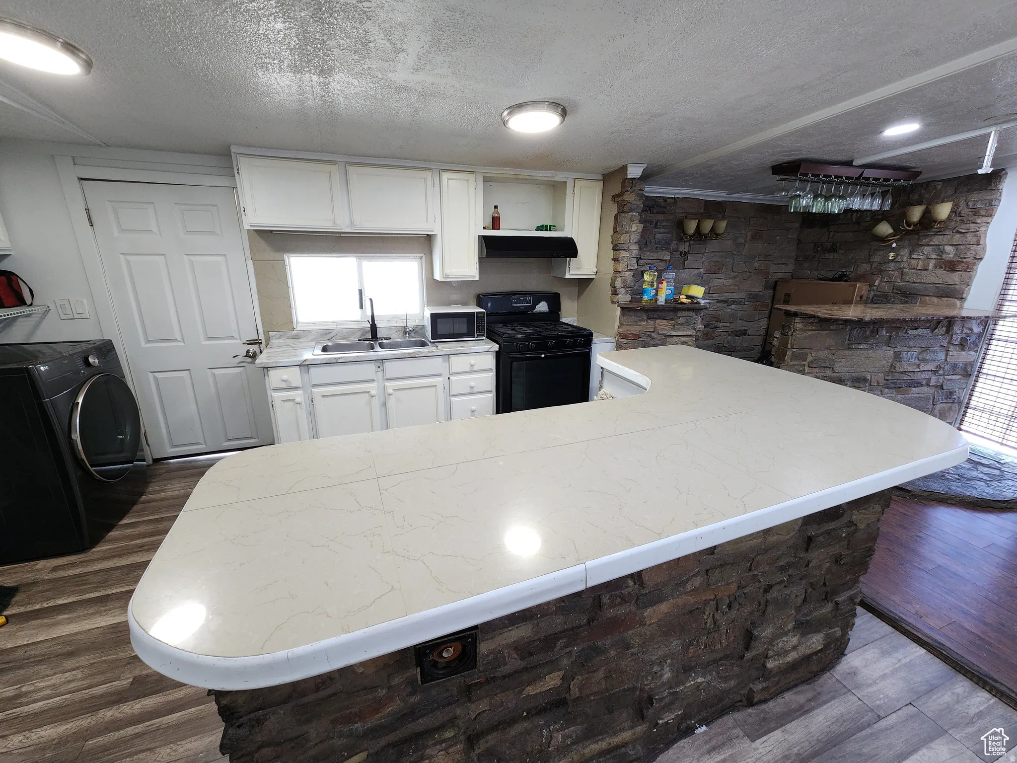 Kitchen island with a light-toned countertop and stacked stone base, complemented by wood-finish flooring