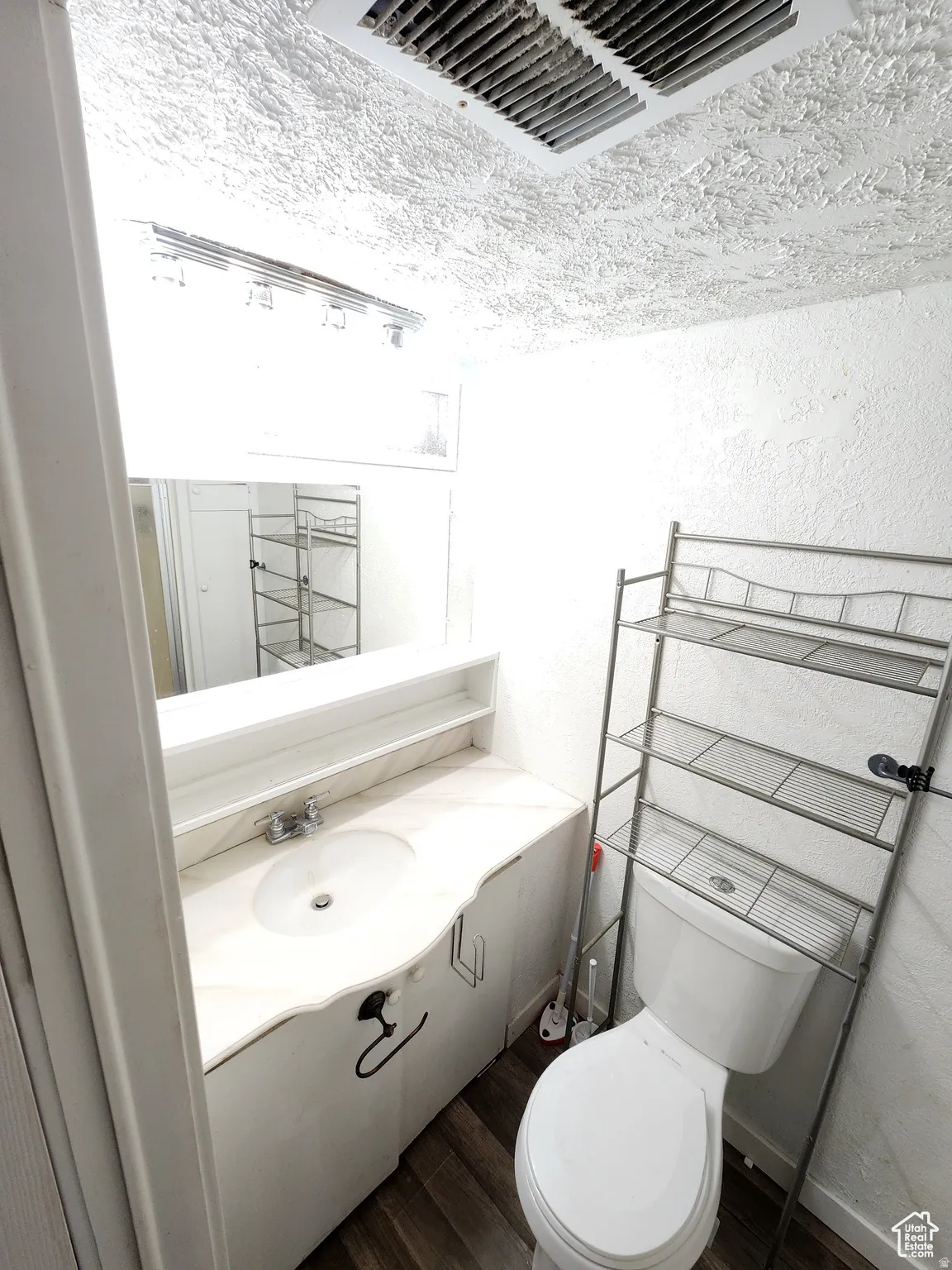 Bathroom featuring a vanity with a drop-in sink, a wall-mounted mirror, and wood-finish flooring