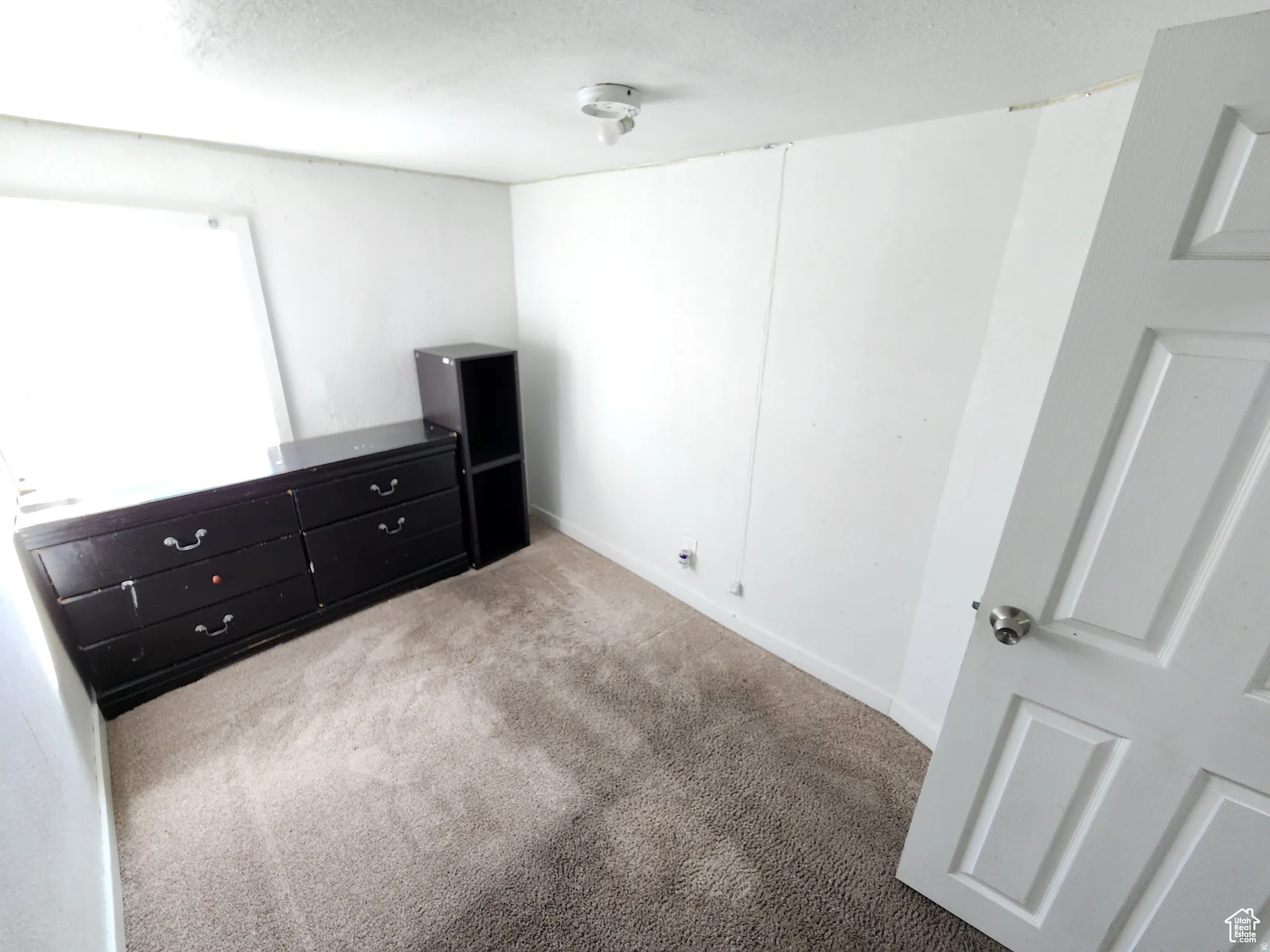 Carpeted room with white walls, a single window, and a white paneled door