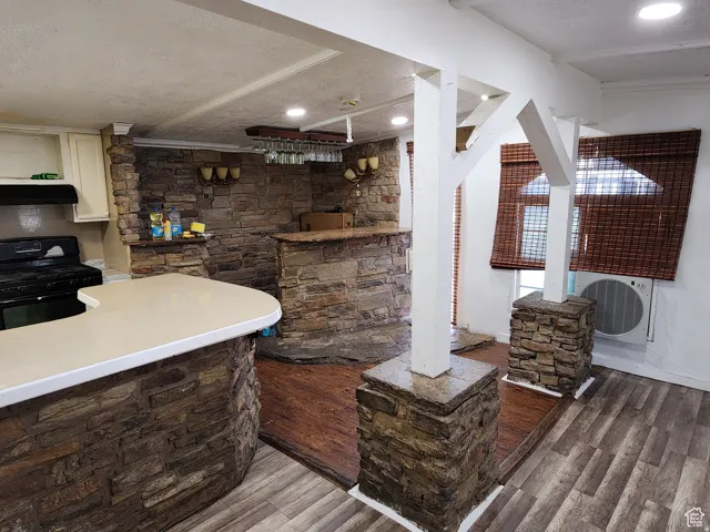 Entertainment area featuring a stone-clad bar with a light-toned countertop, wood-finish flooring, recessed lighting, and wall-mounted sconces