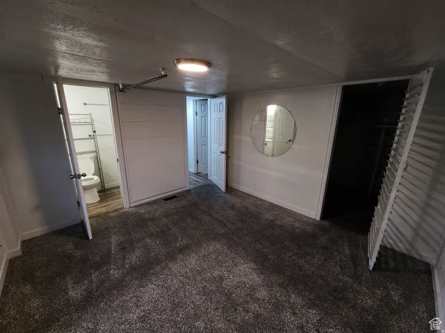 Carpeted room featuring a white interior door, a round wall-mounted mirror, a louvered bi-fold door, and a flush-mount ceiling light fixture