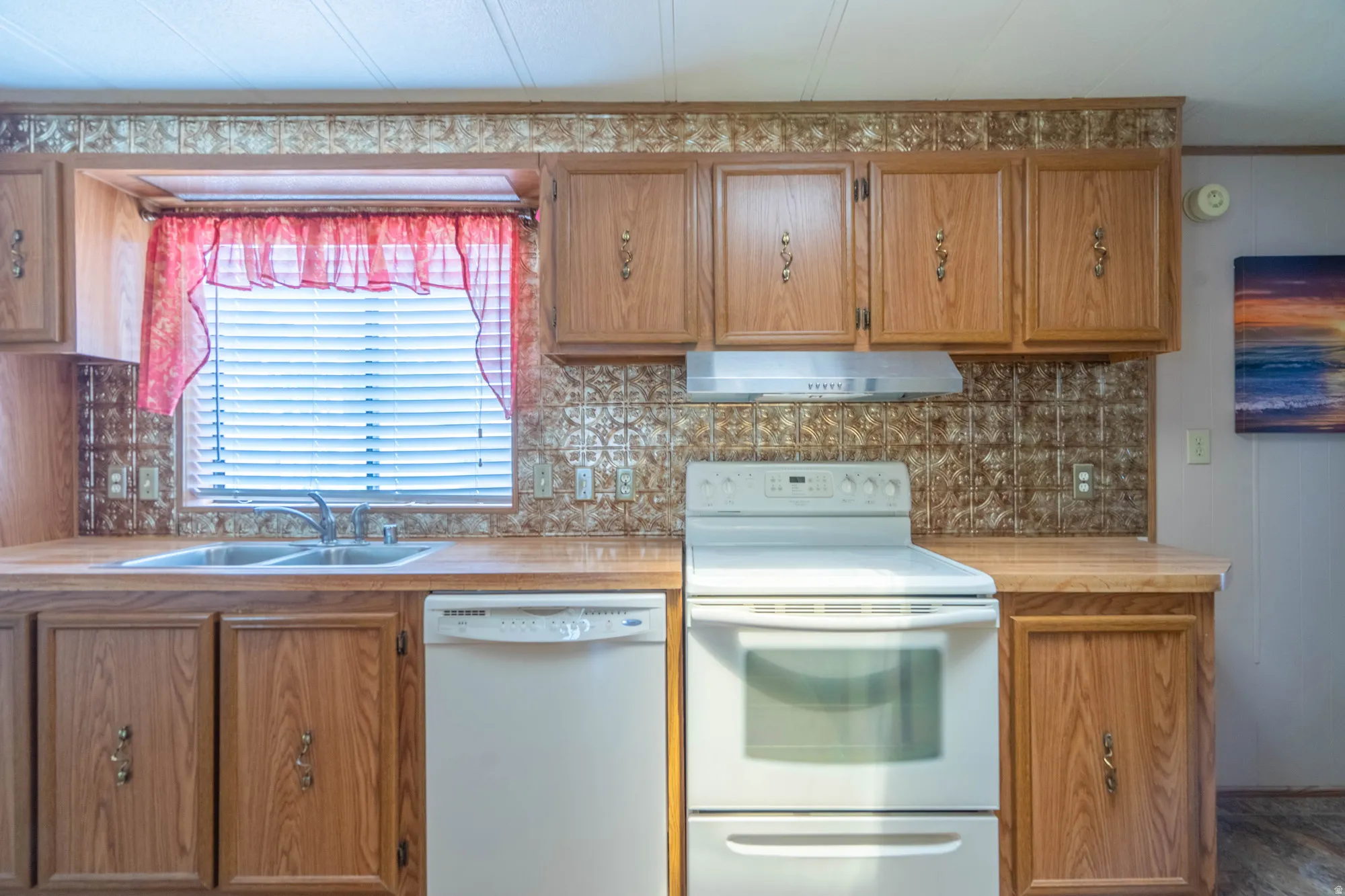 Kitchen featuring wood-finish cabinetry, a double basin stainless steel sink, white dishwasher, white electric range with overhead ventilation, and a patterned backsplash