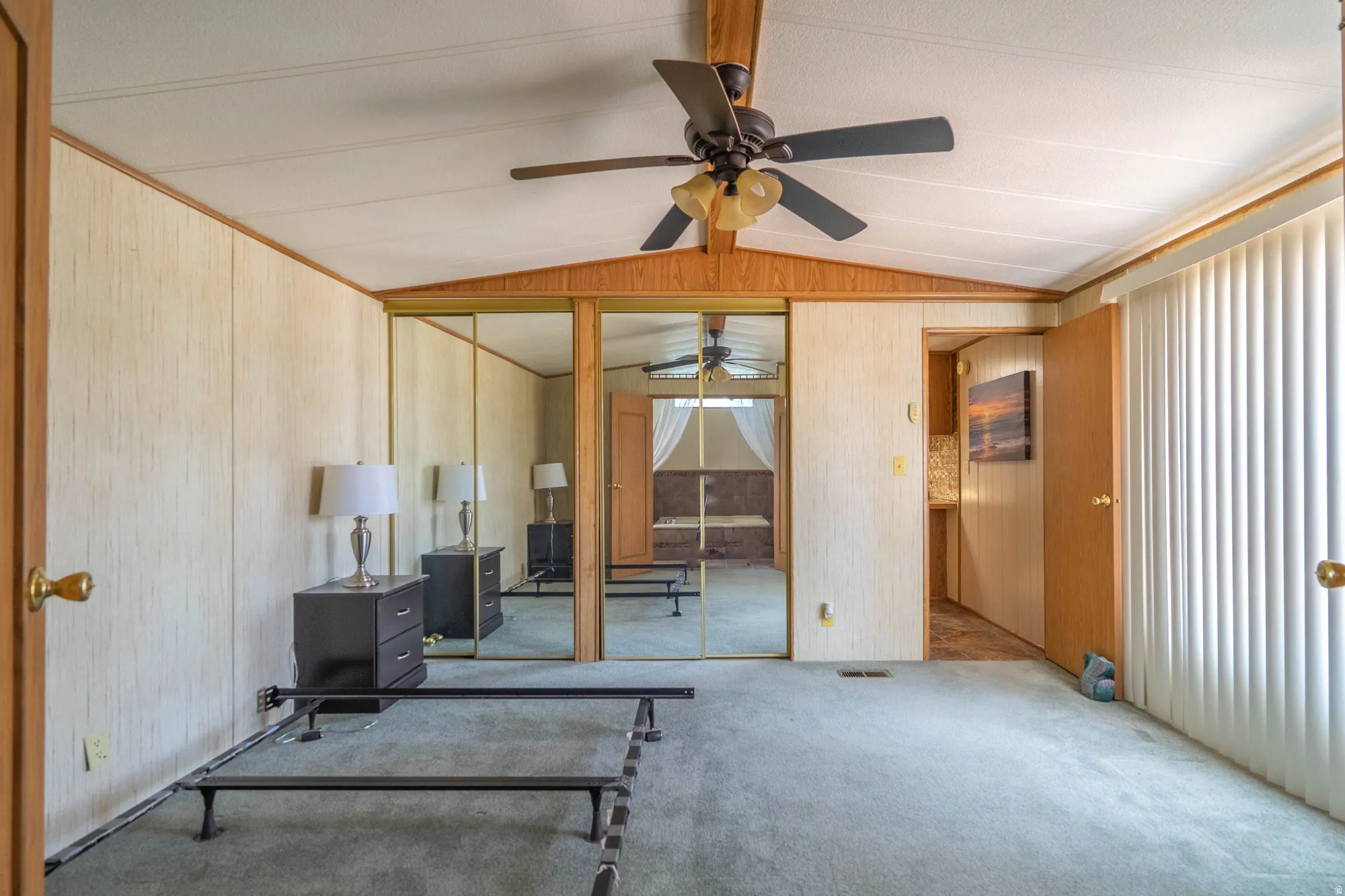 Carpeted room featuring a ceiling fan with light fixture, mirrored sliding closet doors, vertical blinds, and wood-paneled walls