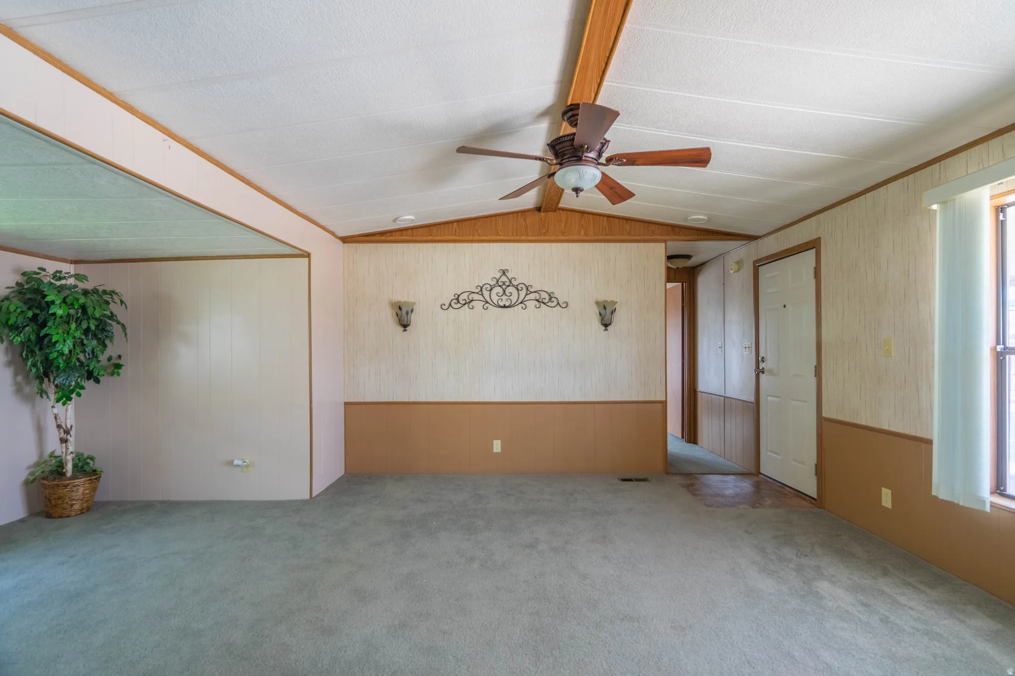 Spacious interior featuring a vaulted ceiling with exposed wood-finish beams, a ceiling fan with integrated lighting, and carpeted flooring