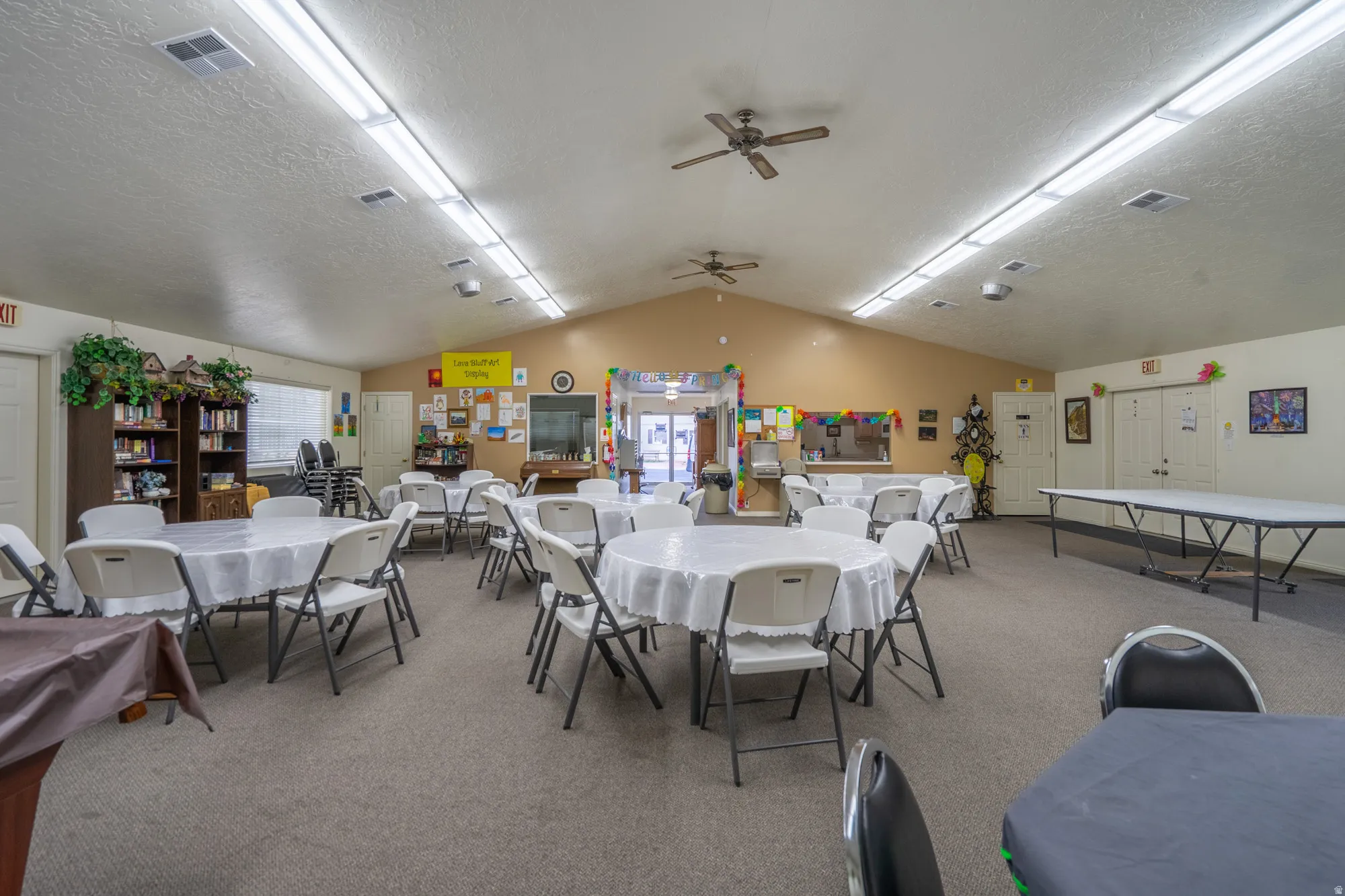 Spacious communal room featuring a vaulted ceiling with multiple ceiling fans and integrated fluorescent lighting