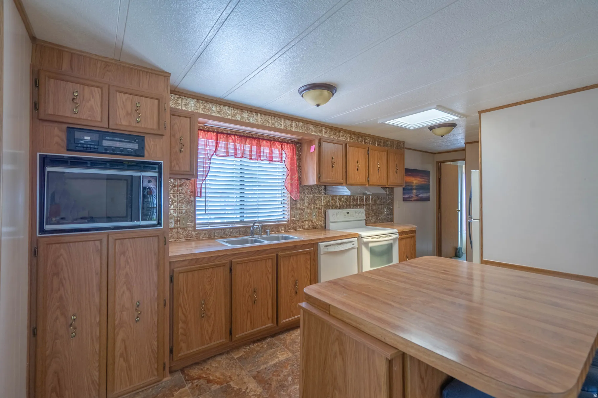 Kitchen featuring wood-finish cabinetry, built-in microwave, double basin sink, and a central island with wood-finish countertop