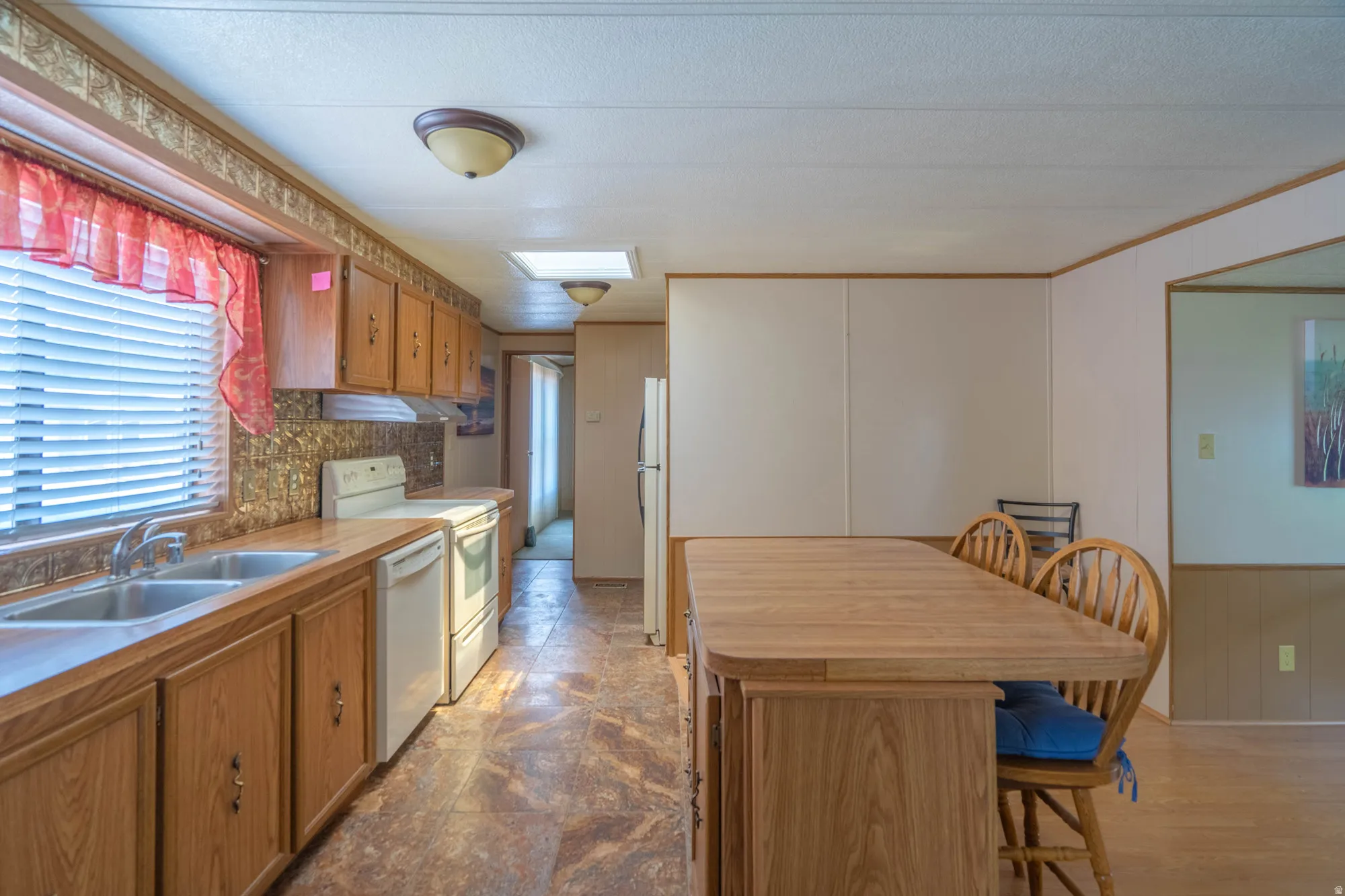 Kitchen featuring wood-finish cabinetry, a double basin stainless steel sink, and white appliances