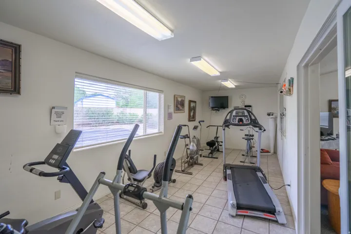 Fitness area featuring tiled flooring, a large window with blinds, and fluorescent overhead lighting