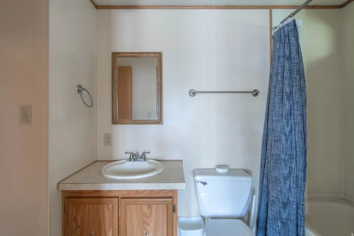 Bathroom featuring a wood-finish vanity with an integrated sink, a framed mirror, and a full-size bathtub with a shower rod