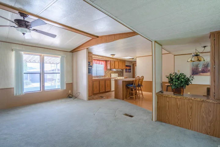 Open concept living area featuring a ceiling fan with integrated lighting, paneled walls, and soft-tone carpeting