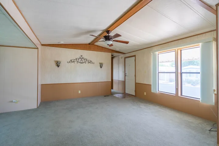 Spacious interior featuring a ceiling fan, light-colored carpeting, multiple windows, and decorative wall sconces