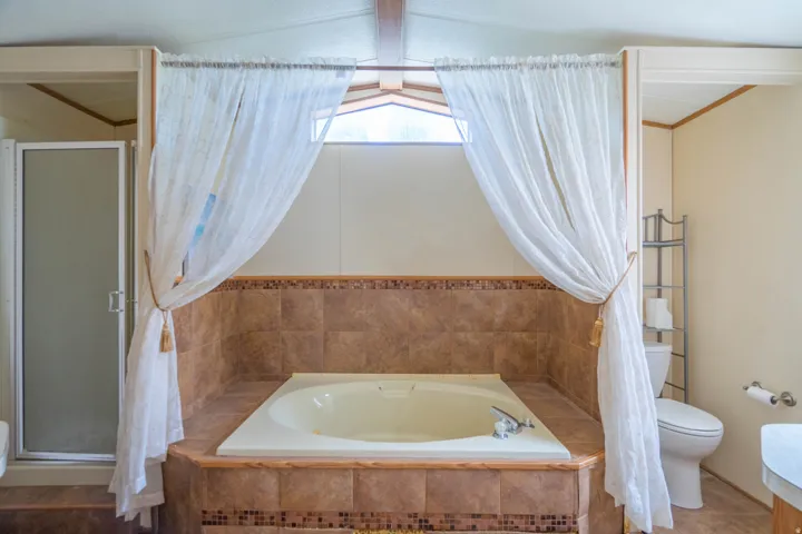 Soaking tub set in a tiled surround with decorative mosaic accents, accompanied by a separate glass-enclosed shower, toilet, and an overhead transom window