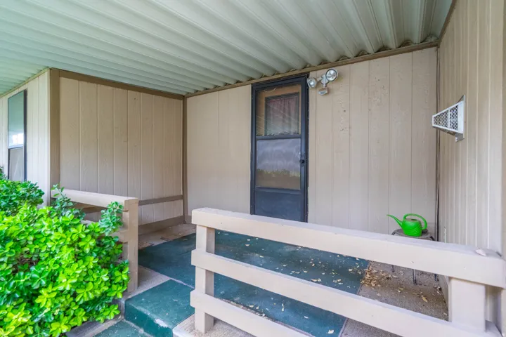 Covered porch with light beige vertical siding and a dark screen door