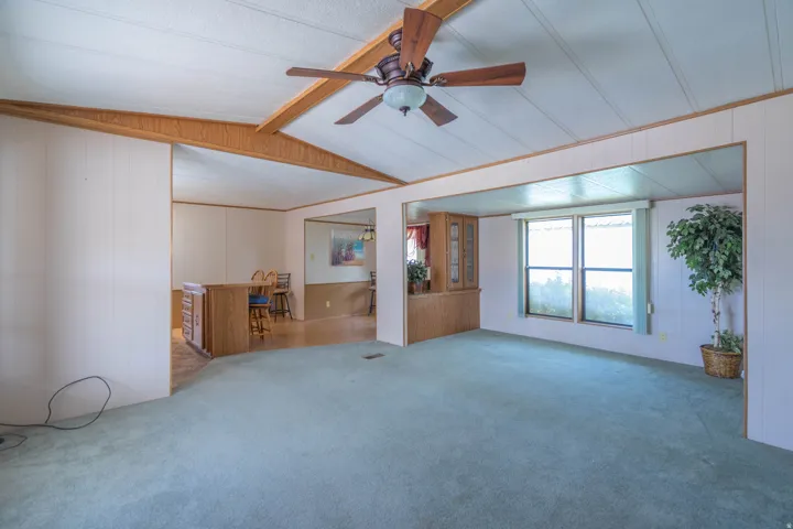 Spacious room featuring vaulted ceilings, a ceiling fan, light blue carpeting, and dual windows