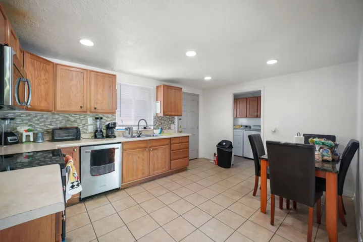 Kitchen featuring light wood cabinetry, a mosaic tile backsplash, white countertops, a stainless steel dishwasher, and recessed lighting