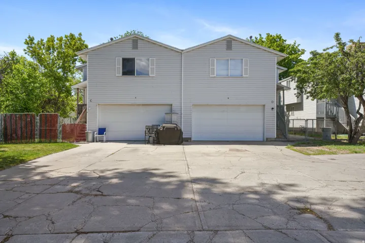 Two-story duplex featuring light gray siding, individual garage doors, and upper-level windows with white shutters