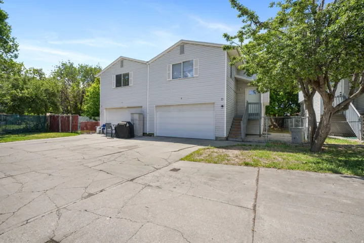 Duplex exterior featuring light gray horizontal siding, multiple garage doors, and individual entry staircases