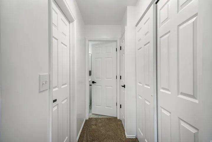 Hallway featuring white paneled doors with black hardware, complementing light-colored walls