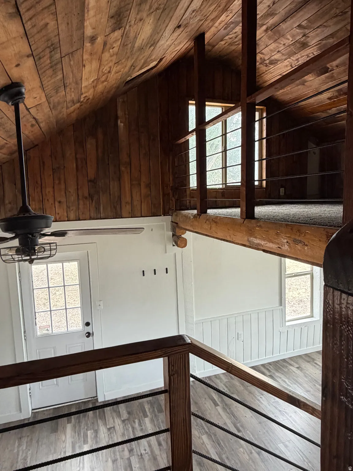 Vaulted wood-paneled ceiling with an exposed beam, wood-finish flooring, white paneled walls, and a multi-pane door
