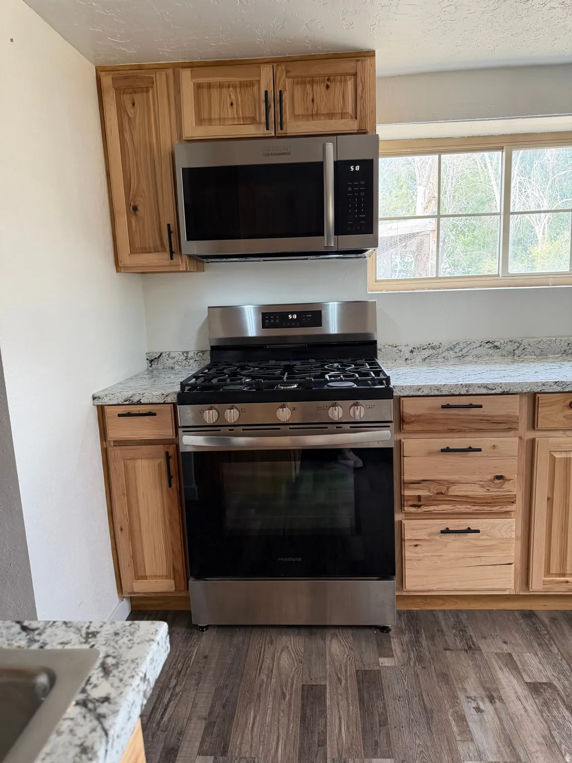 Kitchen featuring wood cabinetry, stainless steel appliances, speckled countertops, and wood-finish flooring