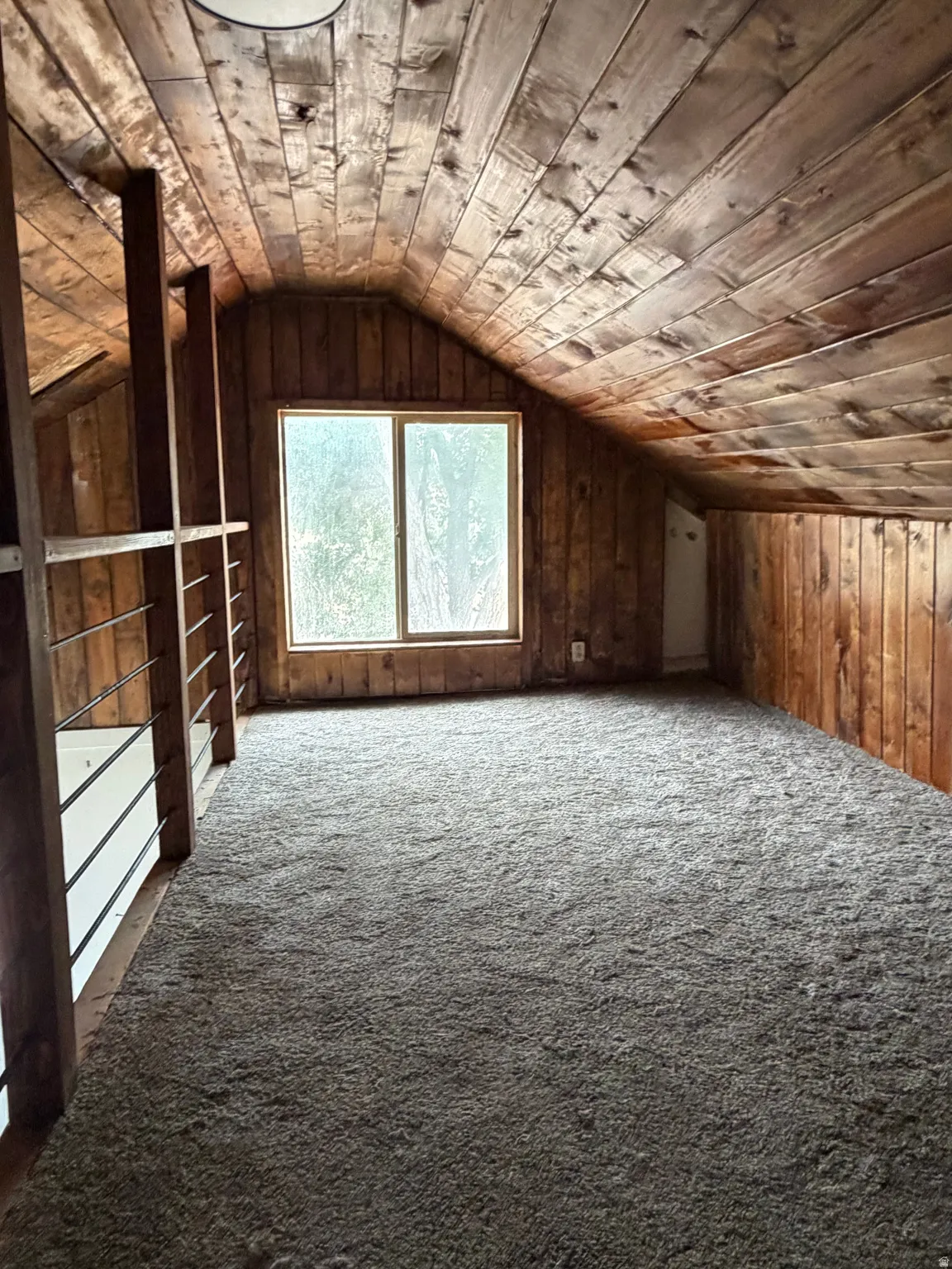 Attic space featuring wood-paneled walls and ceiling, a rectangular window, and wall-to-wall carpeting