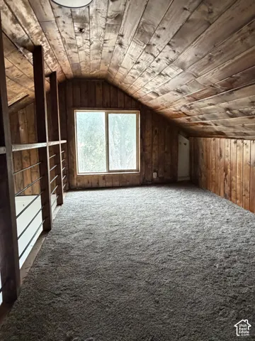 Attic space featuring wood-paneled walls and ceiling, a rectangular window, and wall-to-wall carpeting