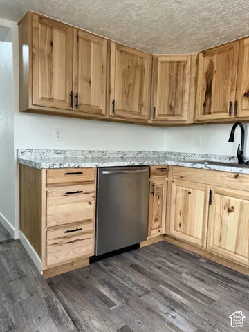 Kitchen featuring natural wood cabinetry with black hardware, light-toned countertops, a stainless steel dishwasher, and wood-finish flooring