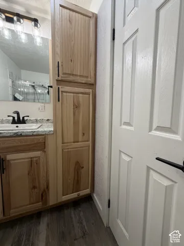 Bathroom vanity with wood-finish cabinetry, a light-colored countertop, and a vessel sink with a dark-finish faucet