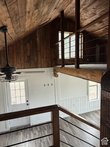 Vaulted wood-paneled ceiling with an exposed beam, wood-finish flooring, white paneled walls, and a multi-pane door