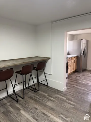 Integrated breakfast bar with wood-finish countertop, wood-finish flooring, and recessed kitchen entry