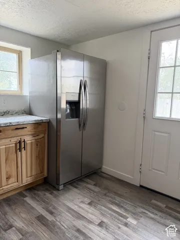 Stainless steel side-by-side refrigerator with an integrated ice and water dispenser, wood-finish flooring, light wood cabinetry with dark hardware, a light-colored countertop, and a white paneled door