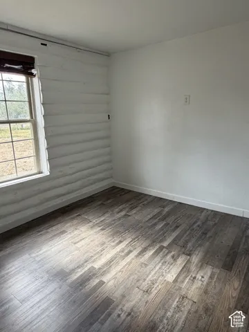 Room featuring wood-finish flooring, white baseboards, a window with grid panes, and a wood-slat window treatment