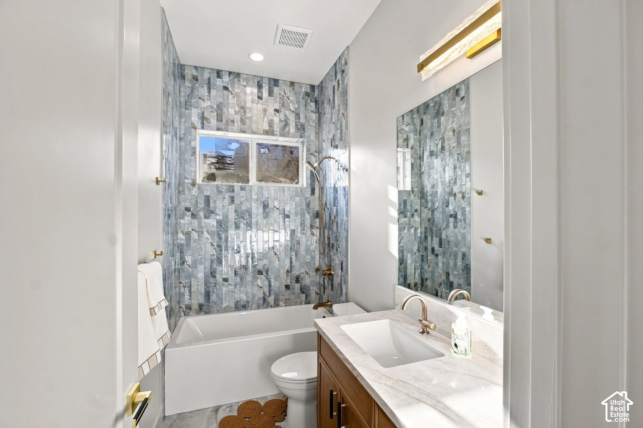 Porcelain bathtub with an iridescent tile surround, a single window, and a vanity featuring a rectangular undermount sink