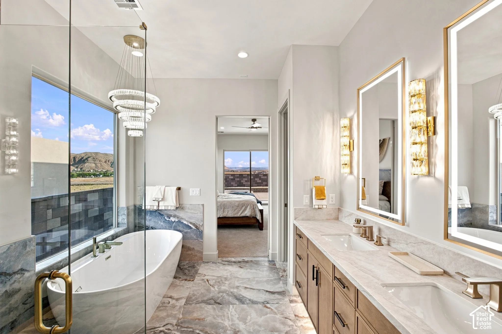 Freestanding soaking tub with a window, dual vanity with undermount sinks, illuminated mirrors, and a glass-enclosed shower
