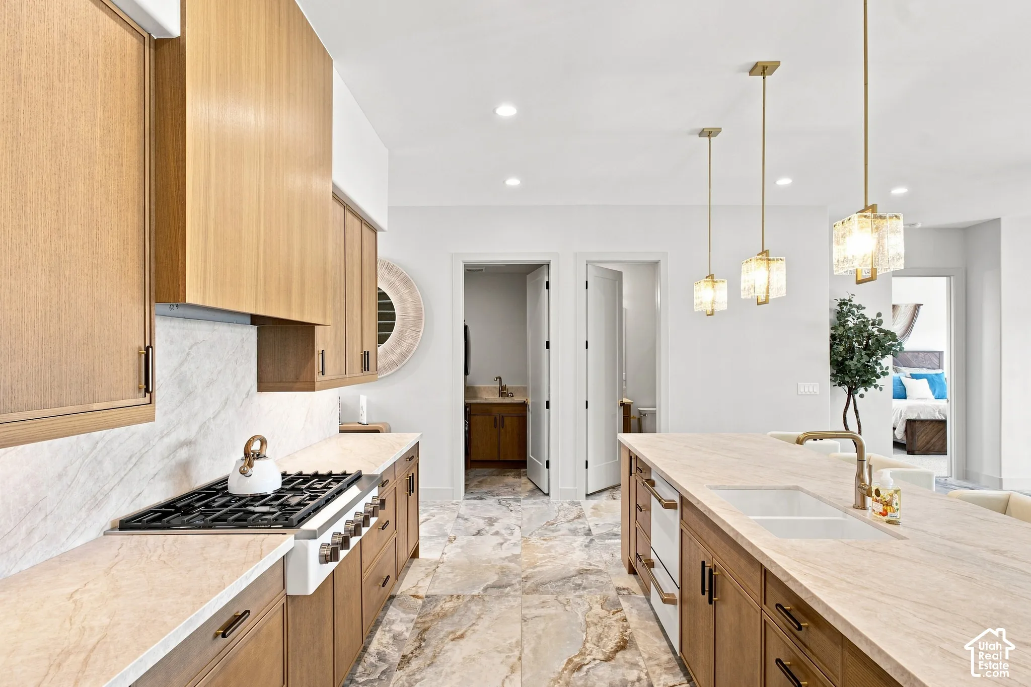 Gourmet kitchen with light wood-finish cabinetry, stone flooring, integrated range, and a large center island with a built-in sink