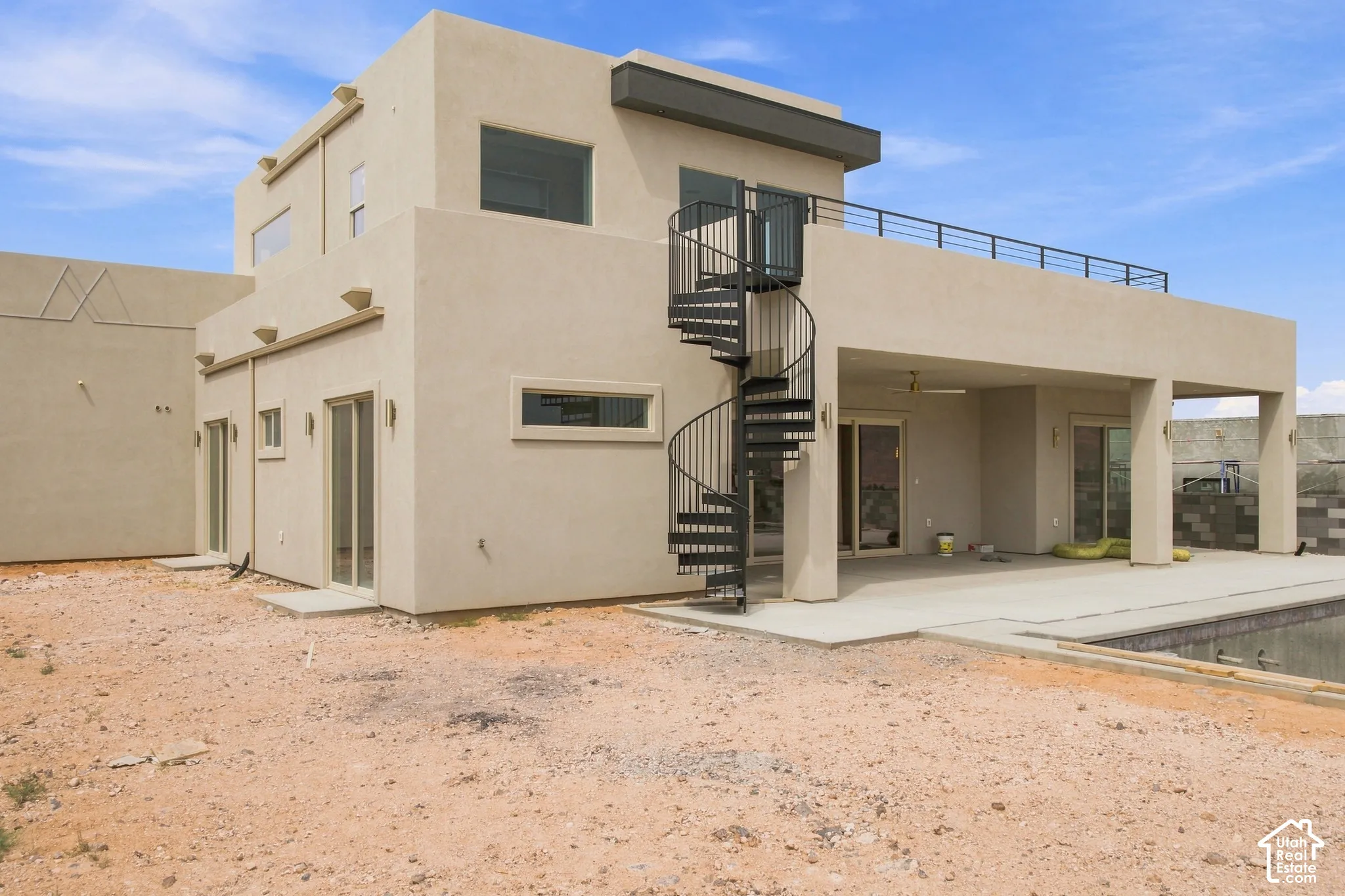 Contemporary stucco exterior with a spiral staircase, upper-level balcony, covered patio, and concrete pool decking