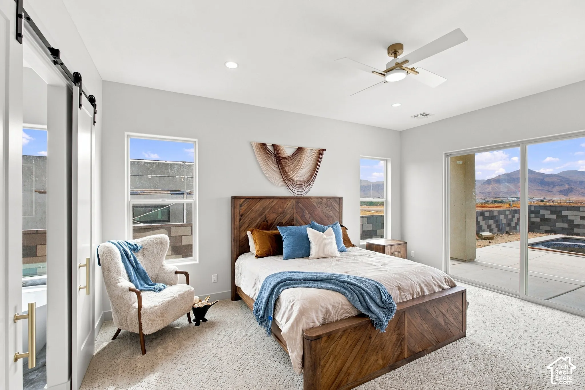 Recessed ceiling lighting, a modern ceiling fan, sliding glass door access to an outdoor patio, and a barn door entry